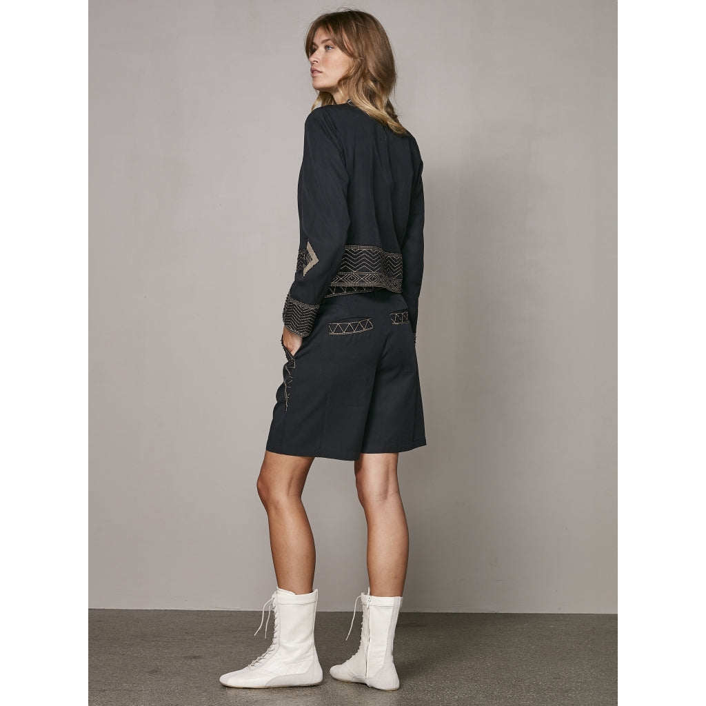 model fra siden med kort sort jakke med broderidetaljer og lynlåslukning. NÜ Zanna Jacket Black