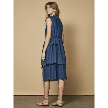 ryggen af model med ærmeløs blå denimkjole med skørt i flere lag. NÜ Ziga denimkjole