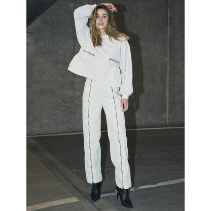 model med bukser og langærmet hvid bluse med ribbet struktur, lynlåslommer foran og en let markeret talje. NÜ Zinne Blouse Bone