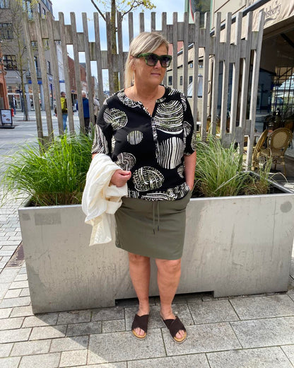 Janni med mønstret bluse og kort grøn nederdel med elastik og snøre i taljen