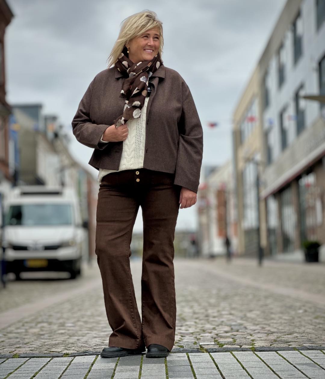 Janni med brun jakke, hvid strik og brune bukser og brunt tørklæde