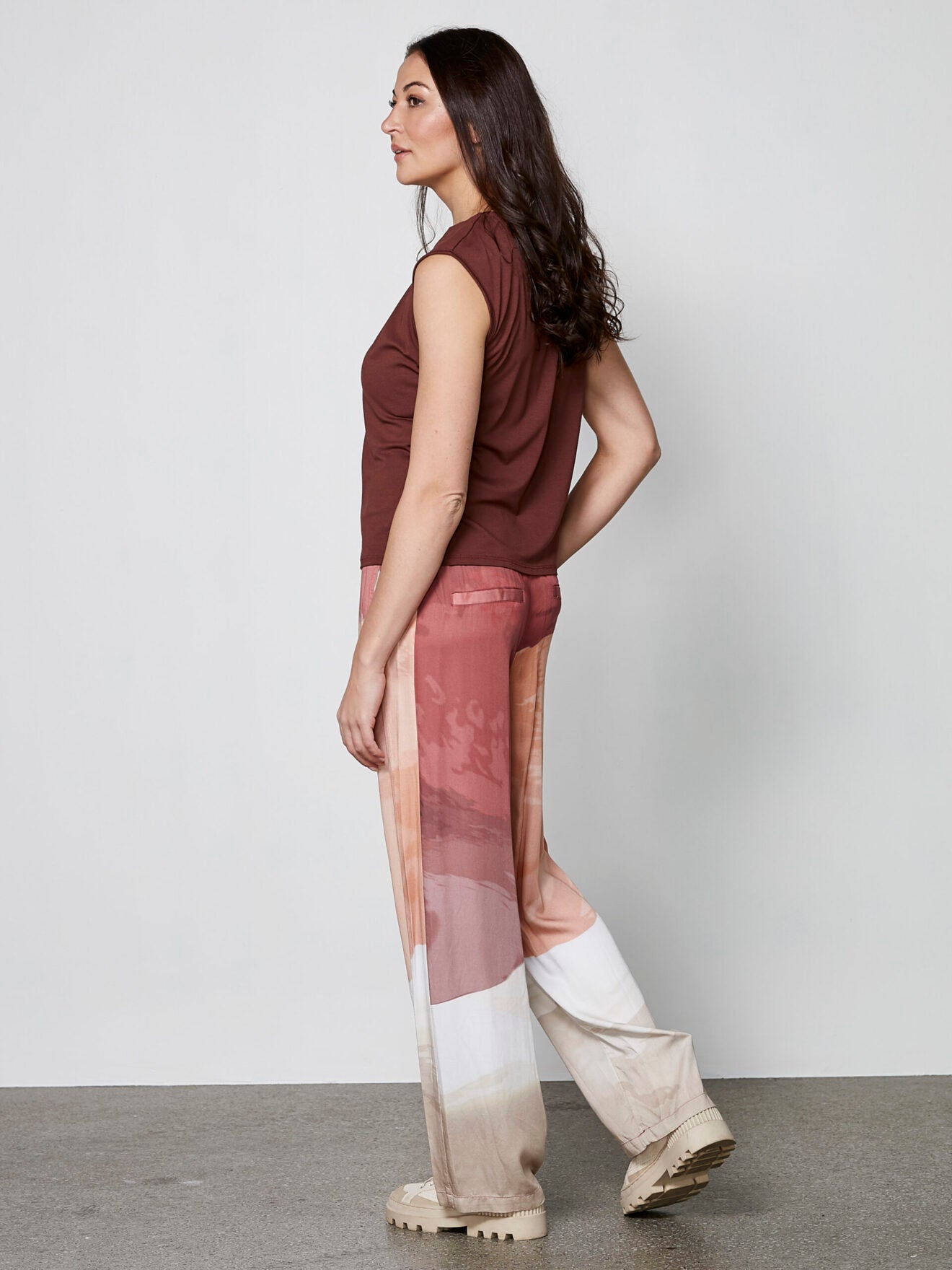 model fra siden med mønstrede bukser i røde og lyse nuancer med sidelommer og elastik i taljen. NÜ Elina Yola Trousers Berry Red Mix 8306-10