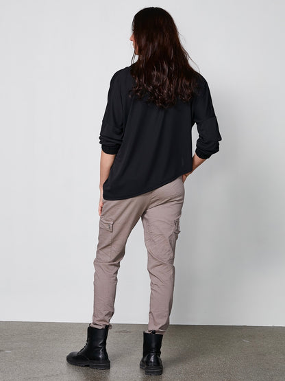 model bagpå med brune bukser med let baggy pasform, elastik i taljen og udvendige lommer på låret. NÜ Carmen Ynde Trousers Mud 8318-10