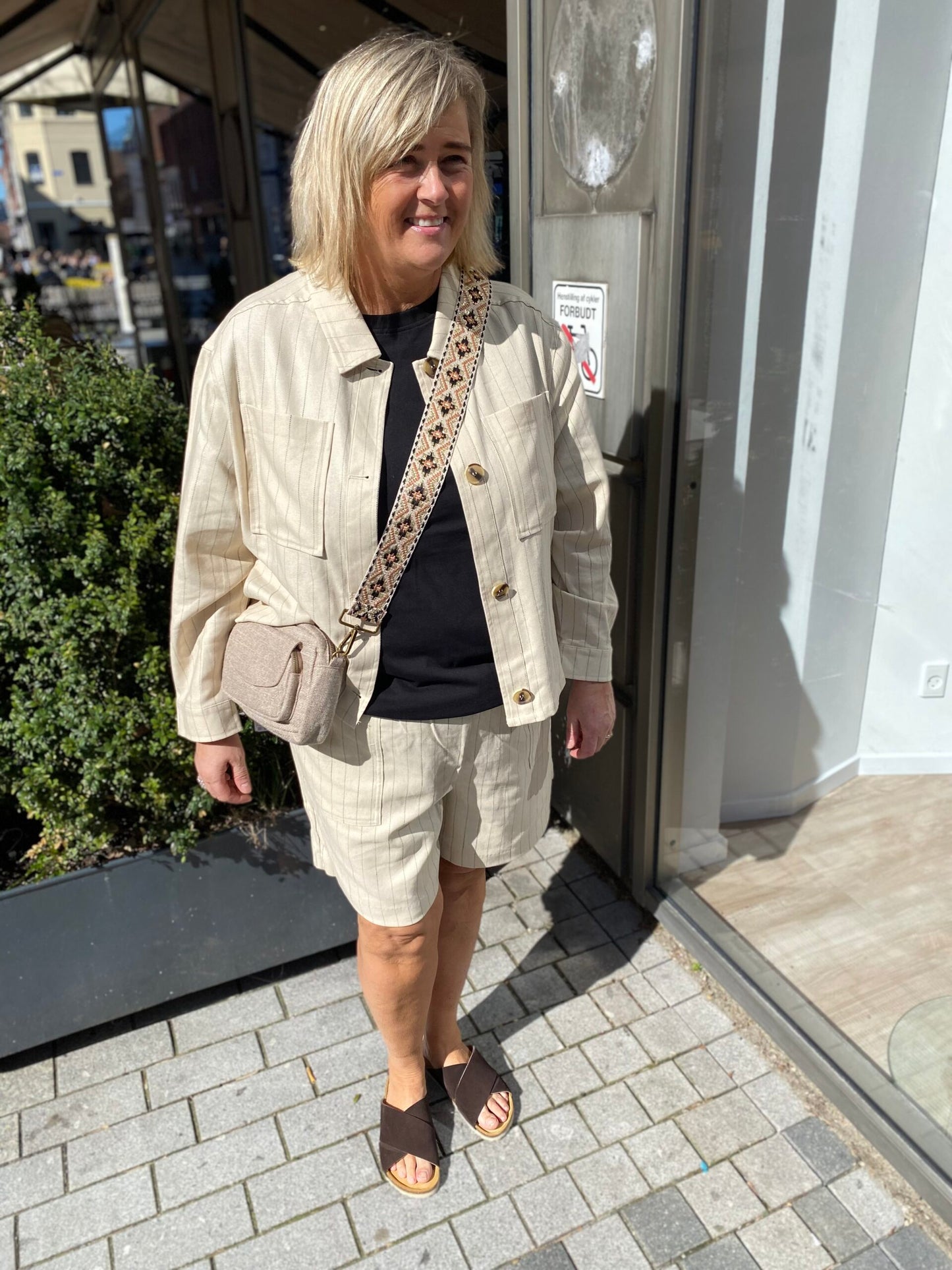 Janni med beige skuldertake og beige shorts med tynde sorte striber.
