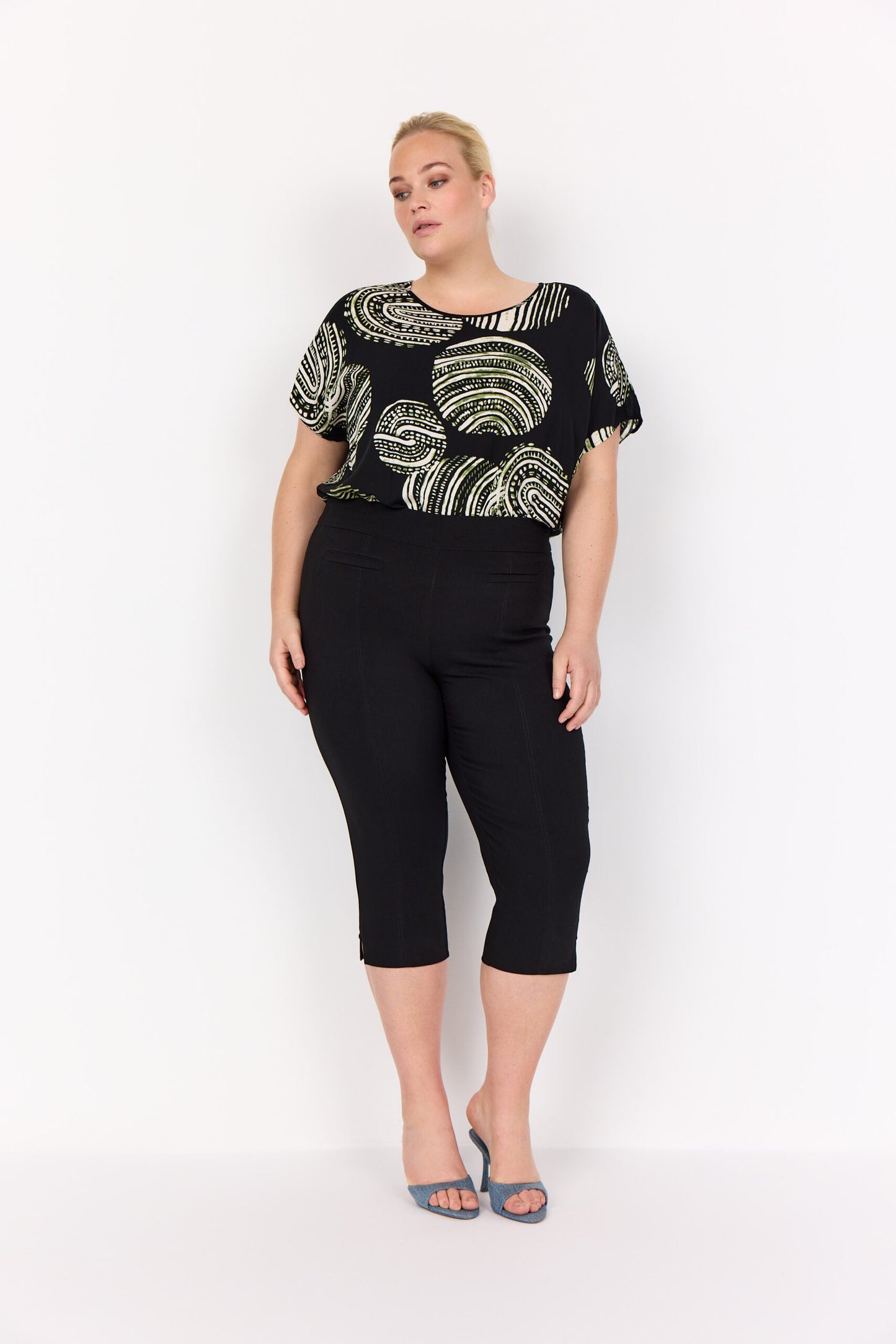 model med sorte bukser og mønstret t-shirt med korte ærmer og rund hals. Wasabi WA-MEDINE 1 T-shirt Black Combi