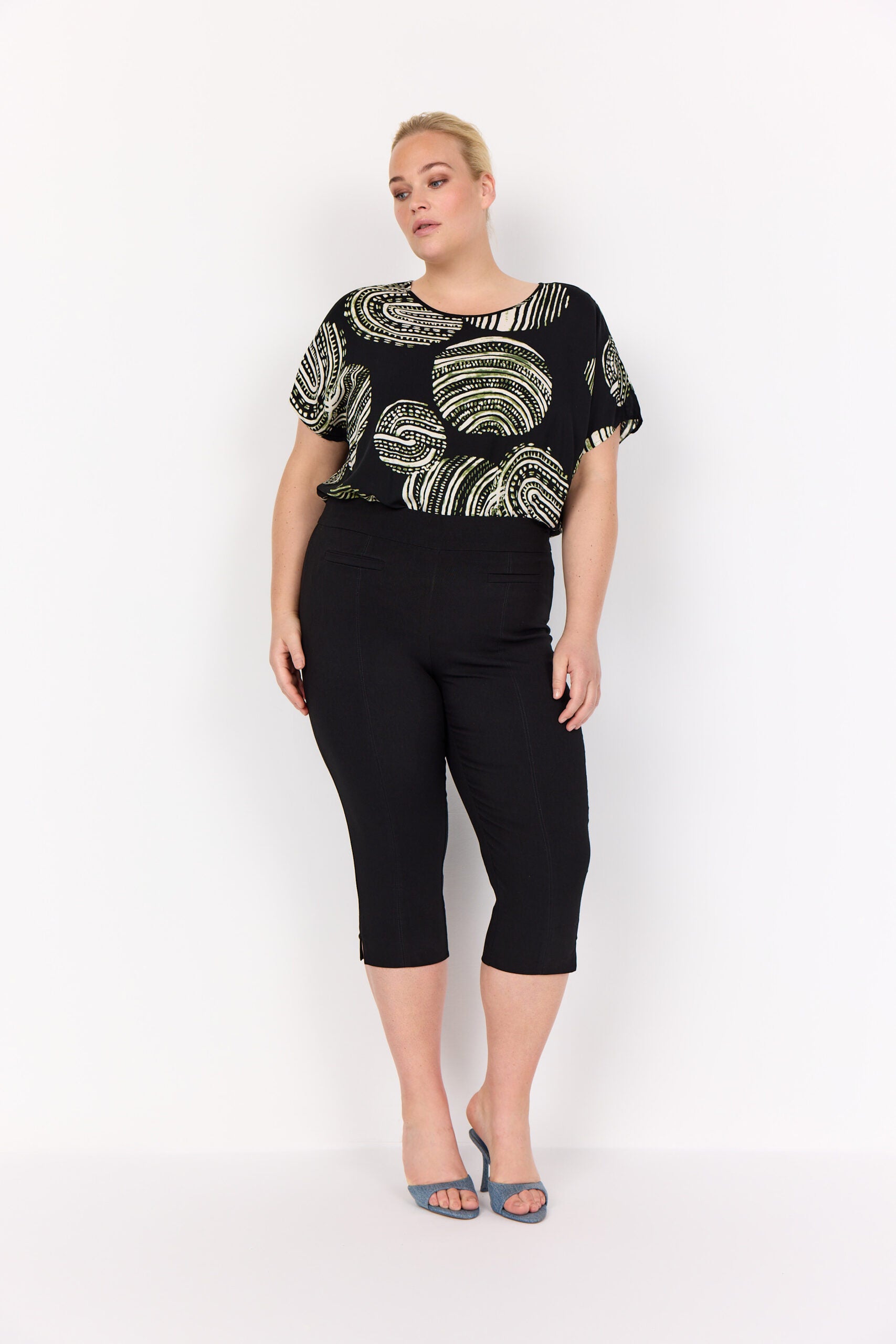 model med sorte bukser og mønstret t-shirt med korte ærmer og rund hals. Wasabi WA-MEDINE 1 T-shirt Black Combi