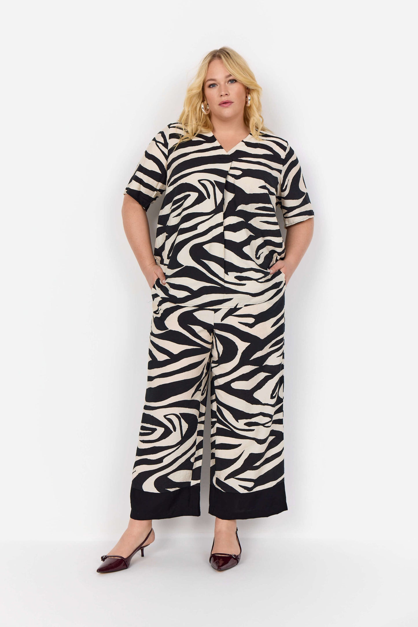 model zebra t-shirt og hænderne i lommerne på bukser med zebraprint og brede sorte kante spå buksebenene. Wasabi WA-LUANA 3 Bukser Black Combi