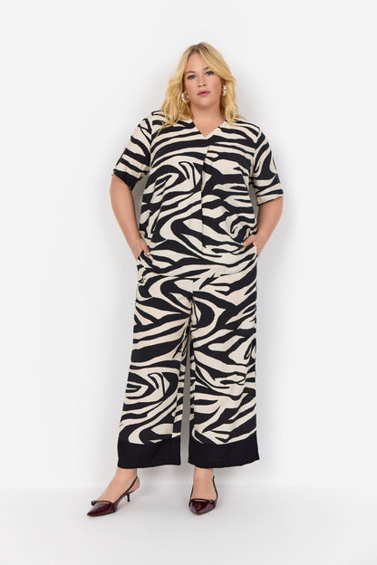 model zebra t-shirt og hænderne i lommerne på bukser med zebraprint og brede sorte kante spå buksebenene. Wasabi WA-LUANA 3 Bukser Black Combi