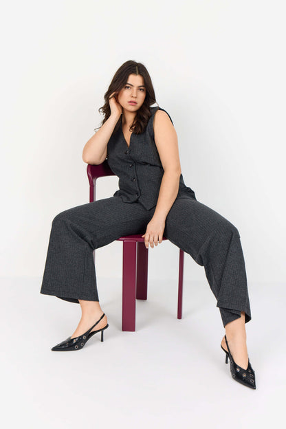 model på stol med mørkegrå bukser med diskrete striber. Wasabi WA-NOIDA 3 Bukser Dark Earth Melange Comb