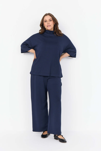 model med blå bukser og afslappet blå bluse med høj hals og bred pasform. Wasabi WA-SABINA 64 Bluse Navy Blazer